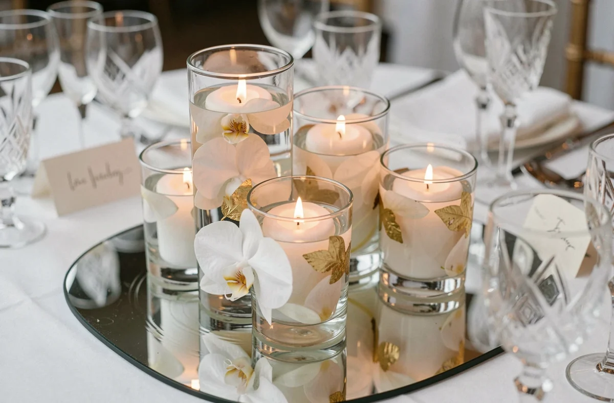 Gros plan sur un centre de table de mariage avec bougies flottantes dans des vases en verre et orchidées blanches